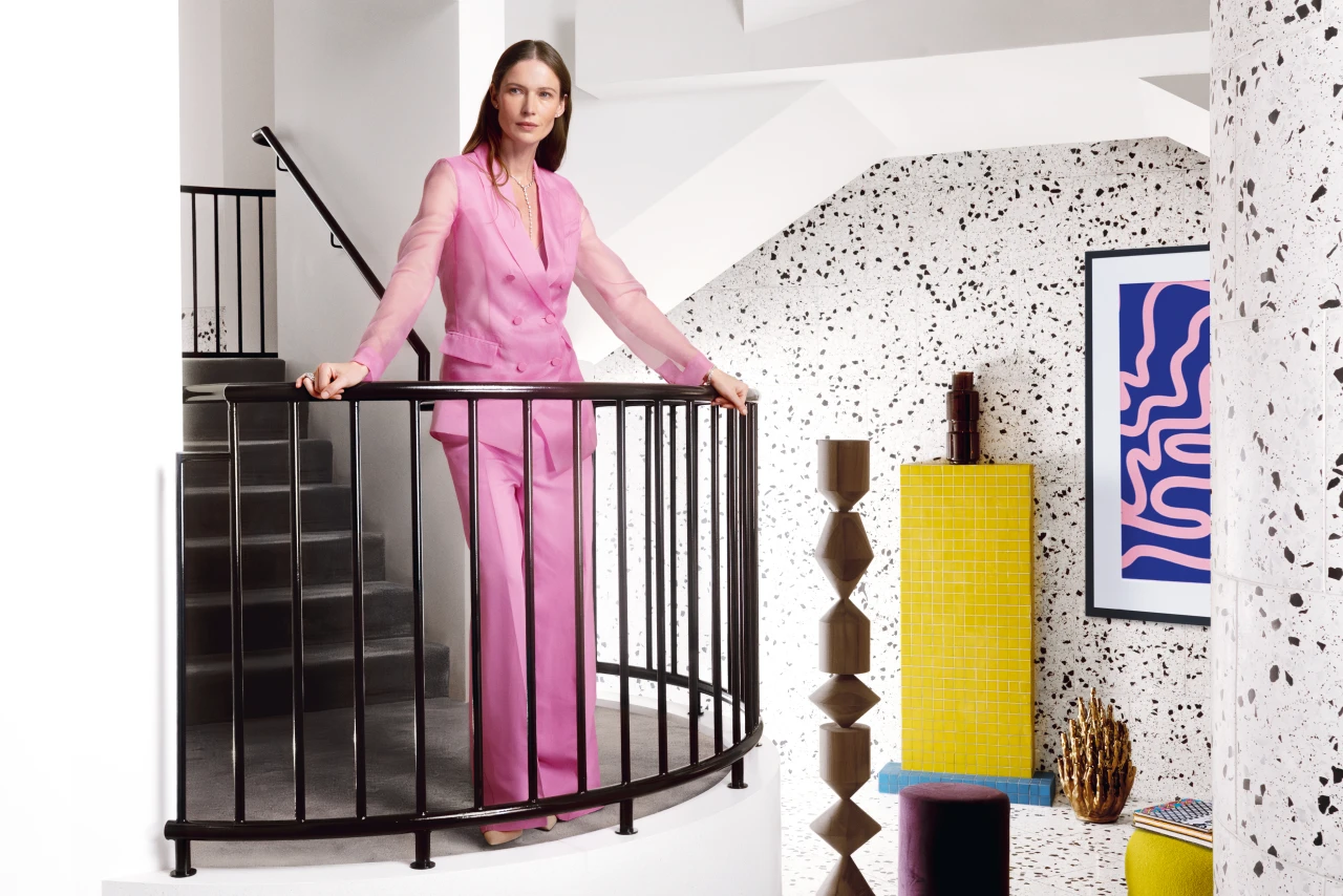 Frau steht an einem Geländer in einem pinken Outfit und schaut nach links. Die Frau trägt Schmuck von Wempe an ihrer Hand und um ihren Hals.