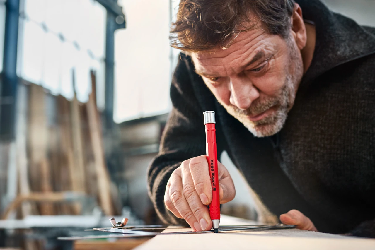 Nahaufnahme von einem Mann welcher mithilfe eines Schmiege-Zirkels und einem edding etwas auf ein Stück Holz zeichnet
