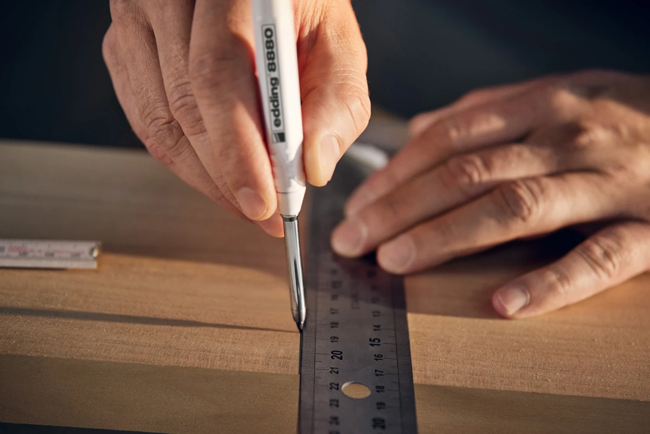 Eine Person zeichnet mit einem Edding eine Schnittlinie auf ein Stück Holz.