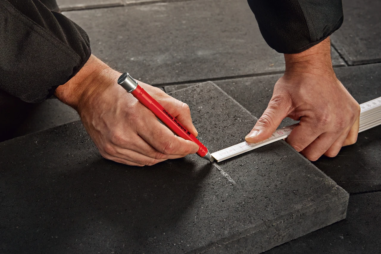 Eine Person zeichnet mit einem Edding-Bleistift eine Schnittlinie auf einer Ziegel an.