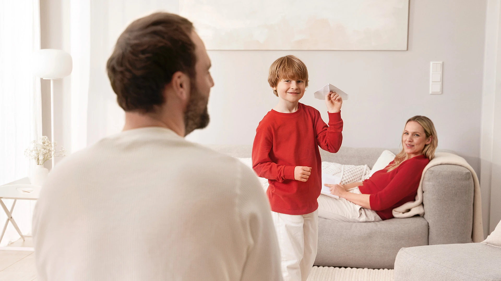 Glückliche Familie in einem Wohnzimmer, Kind hält einen Papierflieger in der Hand