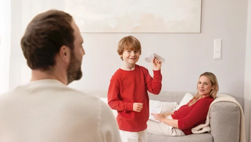 Glückliche Familie sitzt im Wohnzimmer, das Kind wirft einen Papierflieger 