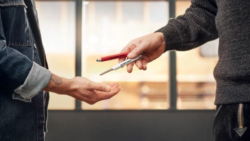 Ein Bild auf welchem eine Person einer anderen Person zwei edding Stifte überreicht